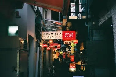 Small street with lit cafe and shop signs above at night