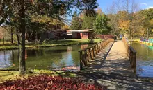 Bridge over the lake to wooden buidlings with a tree in the foreground. 