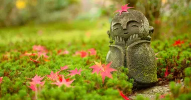 Rotes Ahornblatt auf einer kleinen buddhistischen Mönchsstatue (Jizo) im japanischen Garten