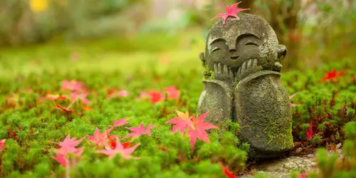 Feuille d'érable sur une petite sculpture de moine dans un jardin japonais